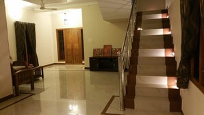 A spacious hallway with a polished floor, a wooden bench, a staircase with a metal railing, and a door leading to another room. - Dvārakā: Luxury Villas of Guruvayur (Guruvayur)
