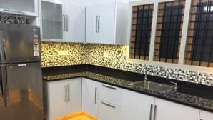 A kitchen with white cabinets, a black countertop, and a tiled backsplash. - Dvārakā: Luxury Villas of Guruvayur (Guruvayur)