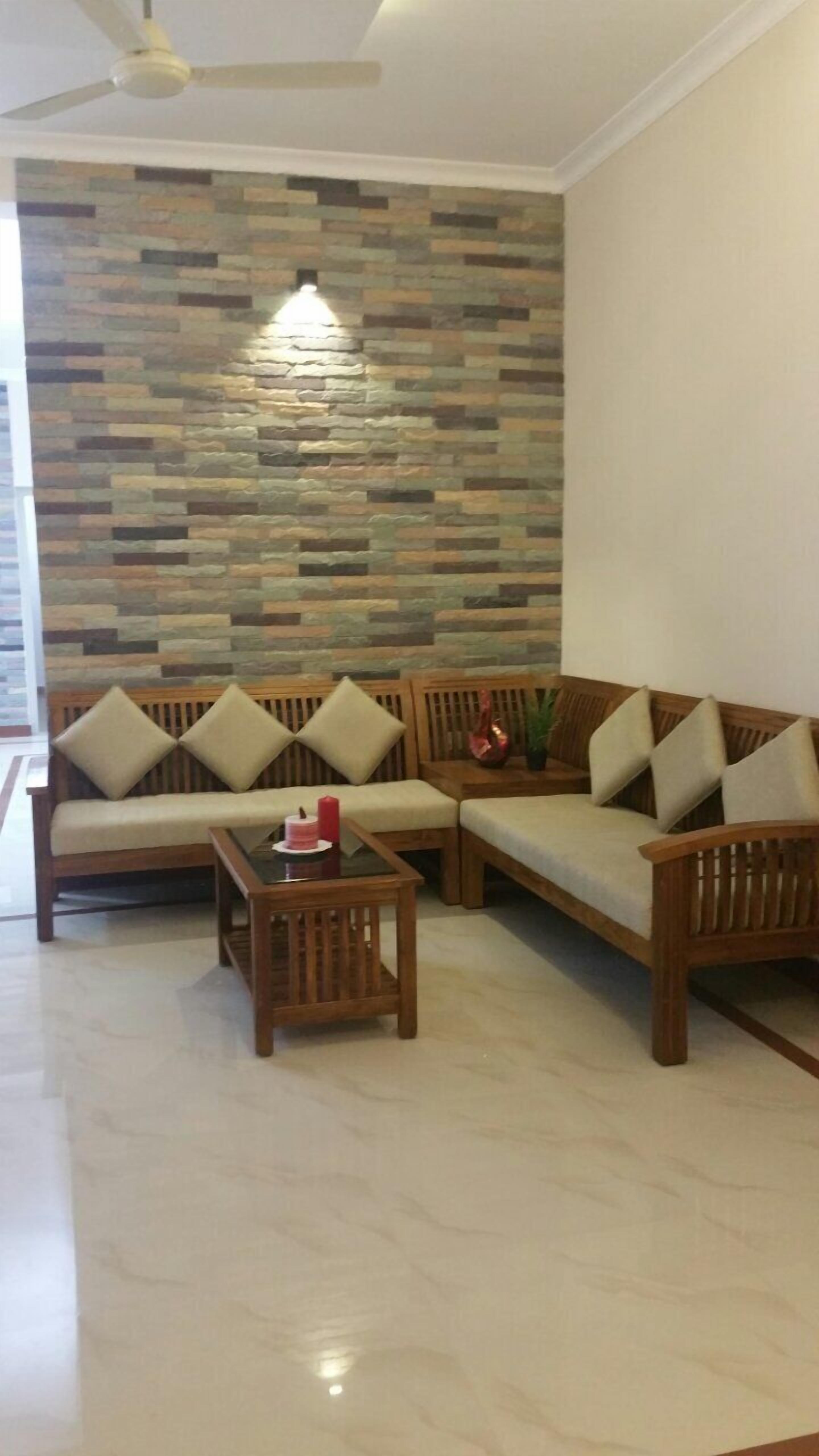 Sala de estar com parede de pedra, ventilador de teto e conjunto de sofá de madeira com almofadas.
