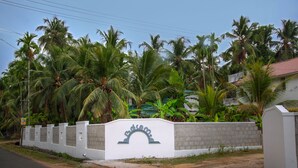 A gated entrance with a sign, surrounded by palm trees and a white wall. - Dvārakā: Luxury Villas of Guruvayur (Guruvayur)