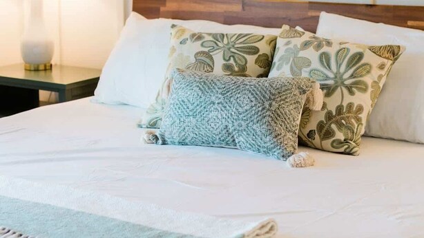 A neatly made bed with a white duvet, two decorative pillows, a bedside lamp, and a nightstand with a lamp. - Luxury Cottage in the Heart of North Georgia (Dahlonega)