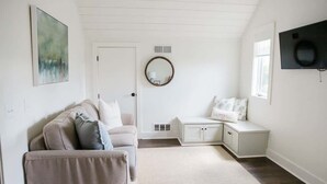 A room with a beige sofa, a white bedside table, a round mirror, and a television mounted on the wall. - Luxury Cottage in the Heart of North Georgia (Dahlonega)