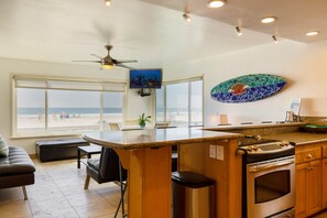 A kitchen with a large island, a ceiling fan, and a view of the beach through large windows.