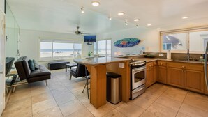Un'ampia cucina con una grande isola, un'area pranzo con vista sulla spiaggia e un soggiorno con divano e TV.