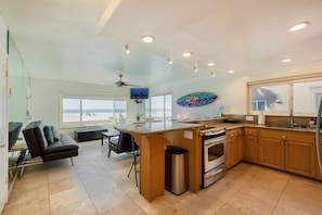 A spacious kitchen with a large island, a dining area with a view of the beach, and a living area with a sofa and a TV. - Right on the Famous Mission Beach Boardwalk - Sleeps up to 18 on Ground Floor - Best location in Mission Beach (San Diego)