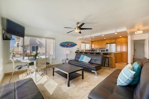 A modern living room with a sofa, coffee table, and a dining area with chairs and a kitchen in the background. - Right on the Famous Mission Beach Boardwalk - Sleeps up to 18 on Ground Floor - Best location in Mission Beach (San Diego)