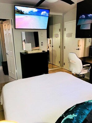 A hotel room with a large bed, a desk with a computer, a chair, and two televisions mounted on the walls. - Right on the Famous Mission Beach Boardwalk - Sleeps 2 on Ground Floor - Best location in Mission Beach (San Diego)