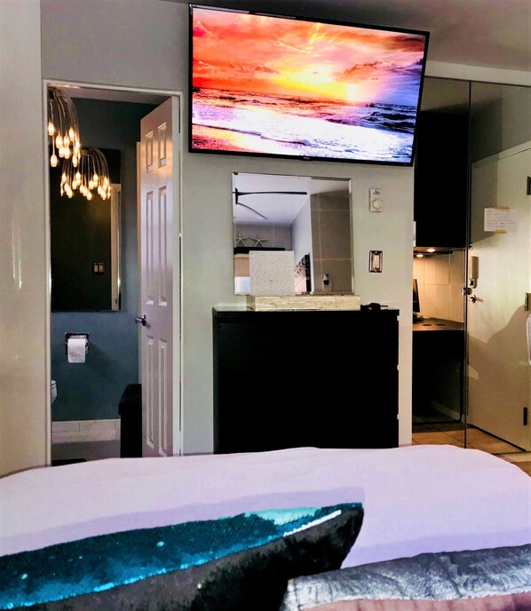 A hotel room with a bed, a TV mounted on the wall, a mirror, and a door leading to another room.
