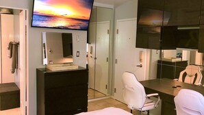 Quarto de hotel com cama, escrivaninha com cadeira, televisão na parede e guarda-roupa.