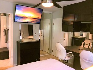 Habitación de hotel con cama, escritorio con silla, televisor montado en la pared y armario.