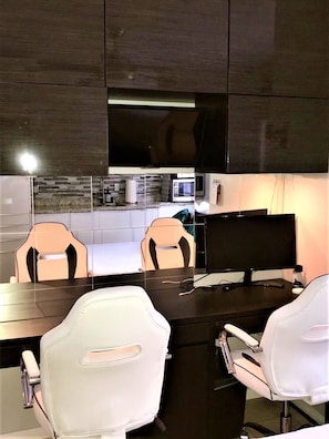A modern kitchen with dark cabinetry, a flat-screen TV, a microwave, and a dining area with white chairs. - Right on the Famous Mission Beach Boardwalk - Sleeps 2 on Ground Floor - Best location in Mission Beach (San Diego)