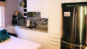 Cozinha compacta com armários brancos, geladeira de aço inoxidável, micro-ondas e painel de azulejos.