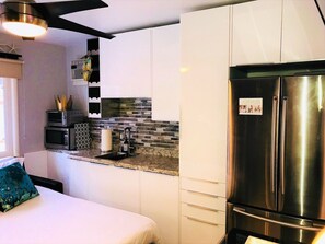 Cocina compacta con gabinetes blancos, refrigerador de acero inoxidable, microondas y salpicadero de azulejos.