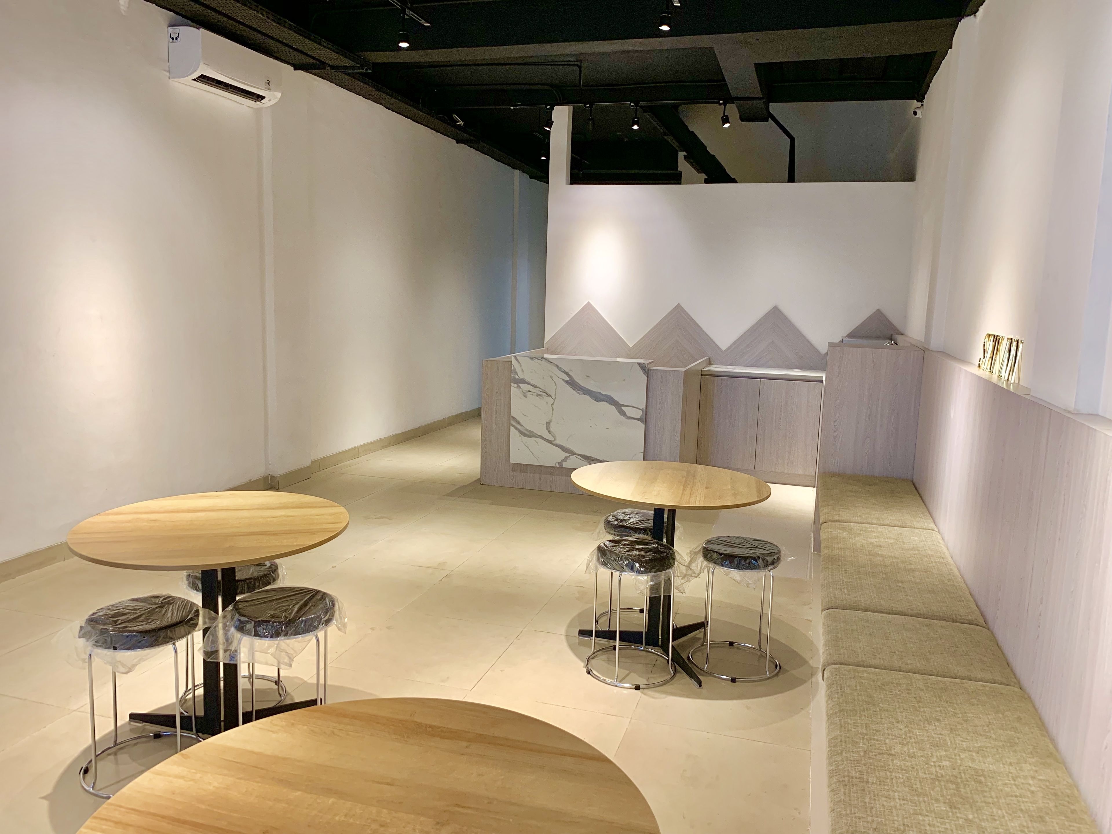 Een modern interieur met ronde tafels en krukken, een marmeren accentmuur en een lichtgekleurde vloer.