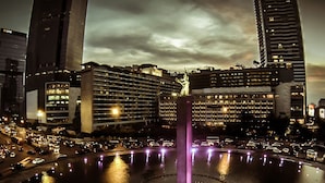 A nighttime cityscape with a prominent building featuring multiple floors and a central fountain. - Stay Inn Hostel Jakarta - Adults only (Jakarta)