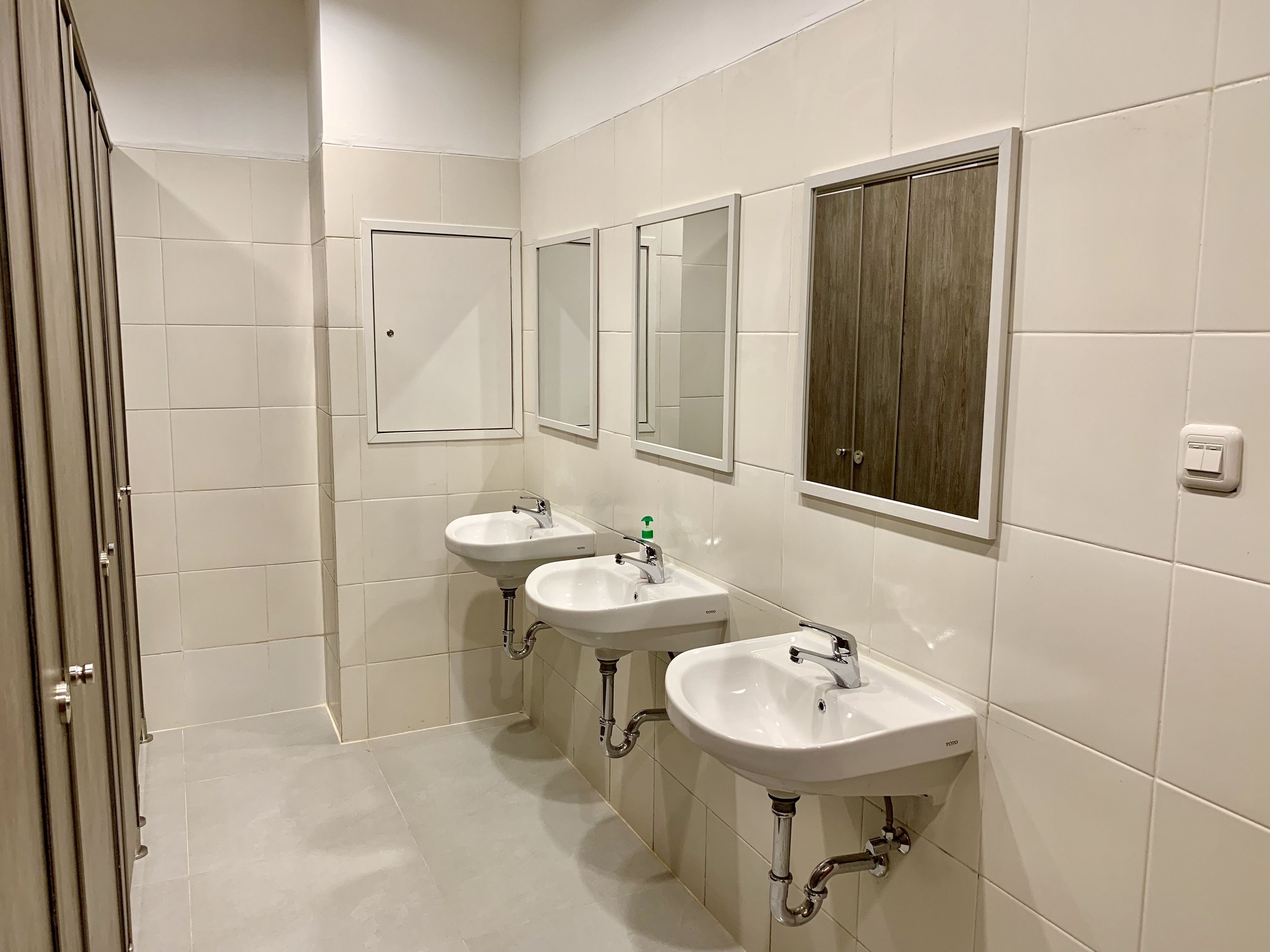 A modern bathroom with three sinks, a mirror, and a wooden panel on the wall.