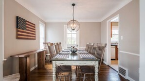 Een eetkamer met een grote houten tafel, stoelen en een hanglamp.