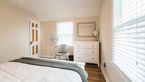 Een slaapkamer met een bed, een dressoir, een stoel, een ventilator en een raam met jaloezieën.
