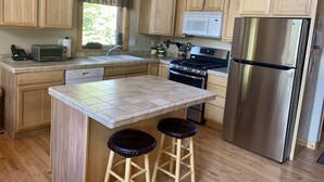 Una cocina con armarios de madera, un refrigerador de acero inoxidable, un microondas, una estufa y un lavavajillas. Hay dos taburetes en la isla.