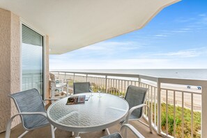 Un balcón con una mesa de vidrio, cuatro sillas y vista a la playa.