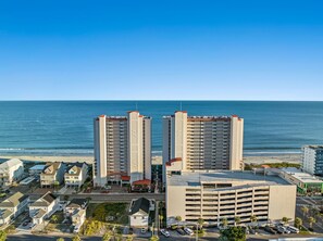Un paisaje urbano costero con dos edificios altos destacados, un estacionamiento y una playa al fondo.