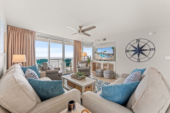 A spacious living room with a view of the ocean, a ceiling fan, and a large compass wall decoration.