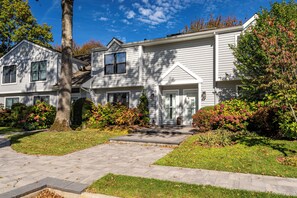 A two-story residential building with a front entrance, a driveway, and surrounding landscaping.