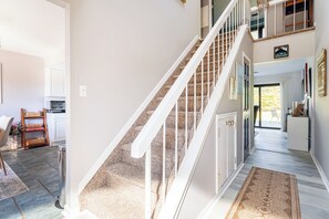 Una escalera con barandillas blancas, un tapete estampado en el suelo y vistas a una habitación con puerta y ventana.