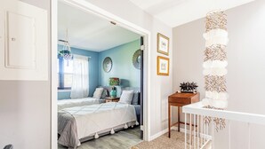 Een slaapkamer met een bed, nachtkastjes, een dressoir, een stoel, een raam met zonwering en een deur.