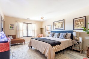 A bedroom with a bed, a nightstand, a chair, a desk, and a window with curtains.