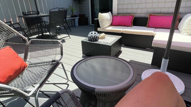 Een terras met rieten meubels, een tafel met glazen blad en een rode parasol.
