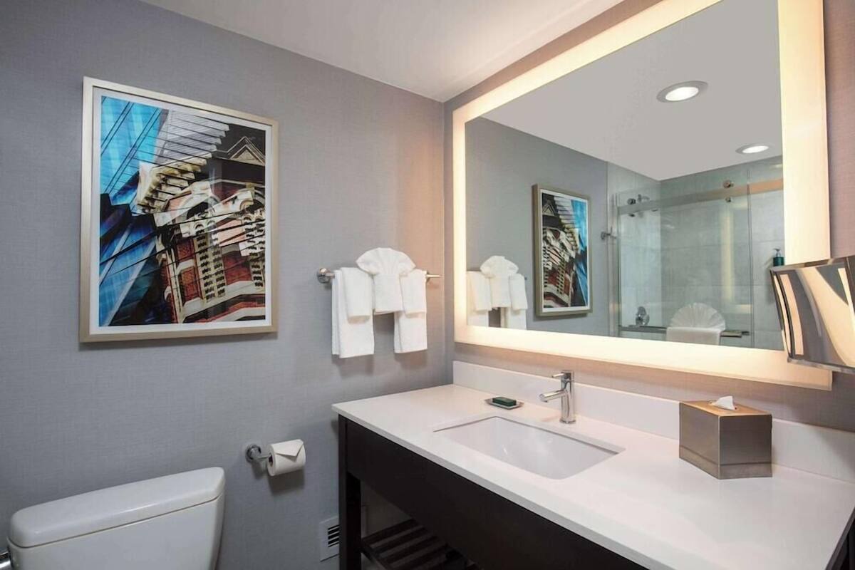 Une salle de bain moderne avec un grand miroir, un lavabo blanc et des toilettes.