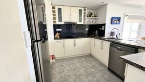 A kitchen with white cabinets, a black dishwasher, and a tiled floor.