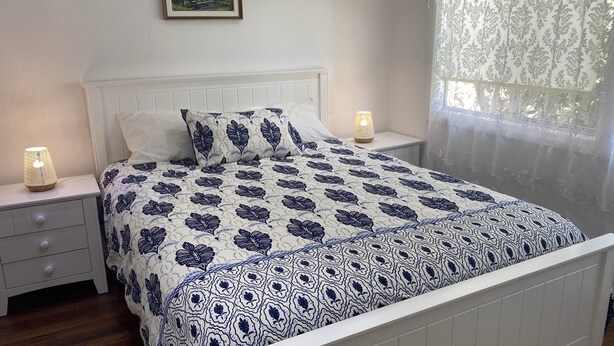 A bedroom with a bed, two bedside tables, a nightstand, a window with sheer curtains, and a wall-mounted picture. - Sand N Salt - spectacular views (Minnie Water)