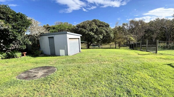 A small, single-story building with a garage door, surrounded by a well-maintained grassy yard and trees. - Sand N Salt - spectacular views (Minnie Water)