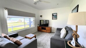 A living room with a large window, a television, a sofa, and a lamp.