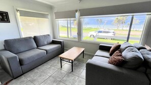 A living room with a grey sofa, a wooden coffee table, and a view of a road with a white car.