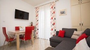 A living room with a grey sofa, red chairs, a dining table, and a TV mounted on the wall. - Split Center Beautiful Apartment (Split)