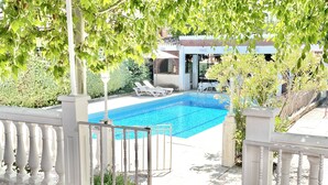 A swimming pool with a white fence, potted plants, and a building in the background. - Villa with private pool, large garden and leisure activities, 20 min from Madrid (Navalcarnero)