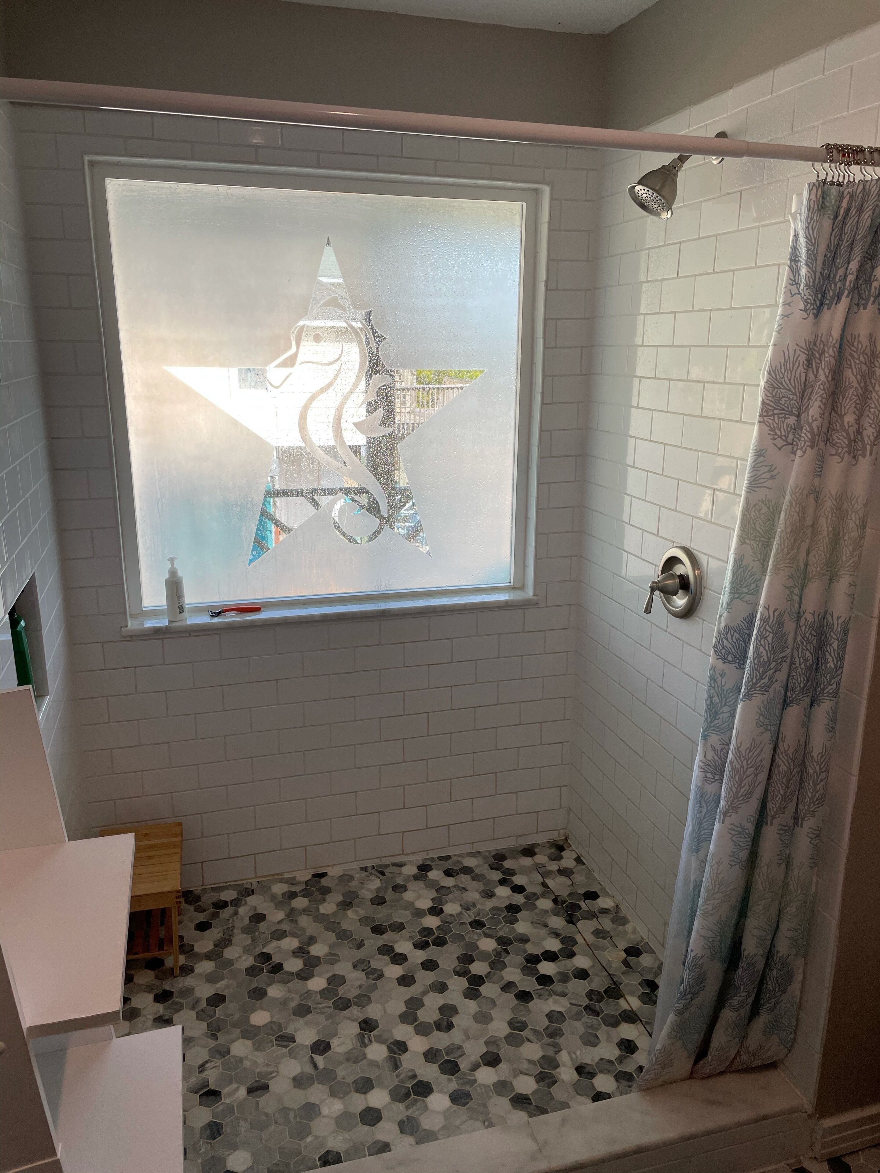 A shower with a frosted window, white tiled walls, and a patterned floor.