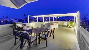 Un patio exterior con una parrilla, mesa de comedor, sillas y una zona de estar cubierta.