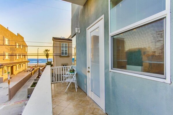 A balcony with a view of the beach, a door, and a window.
