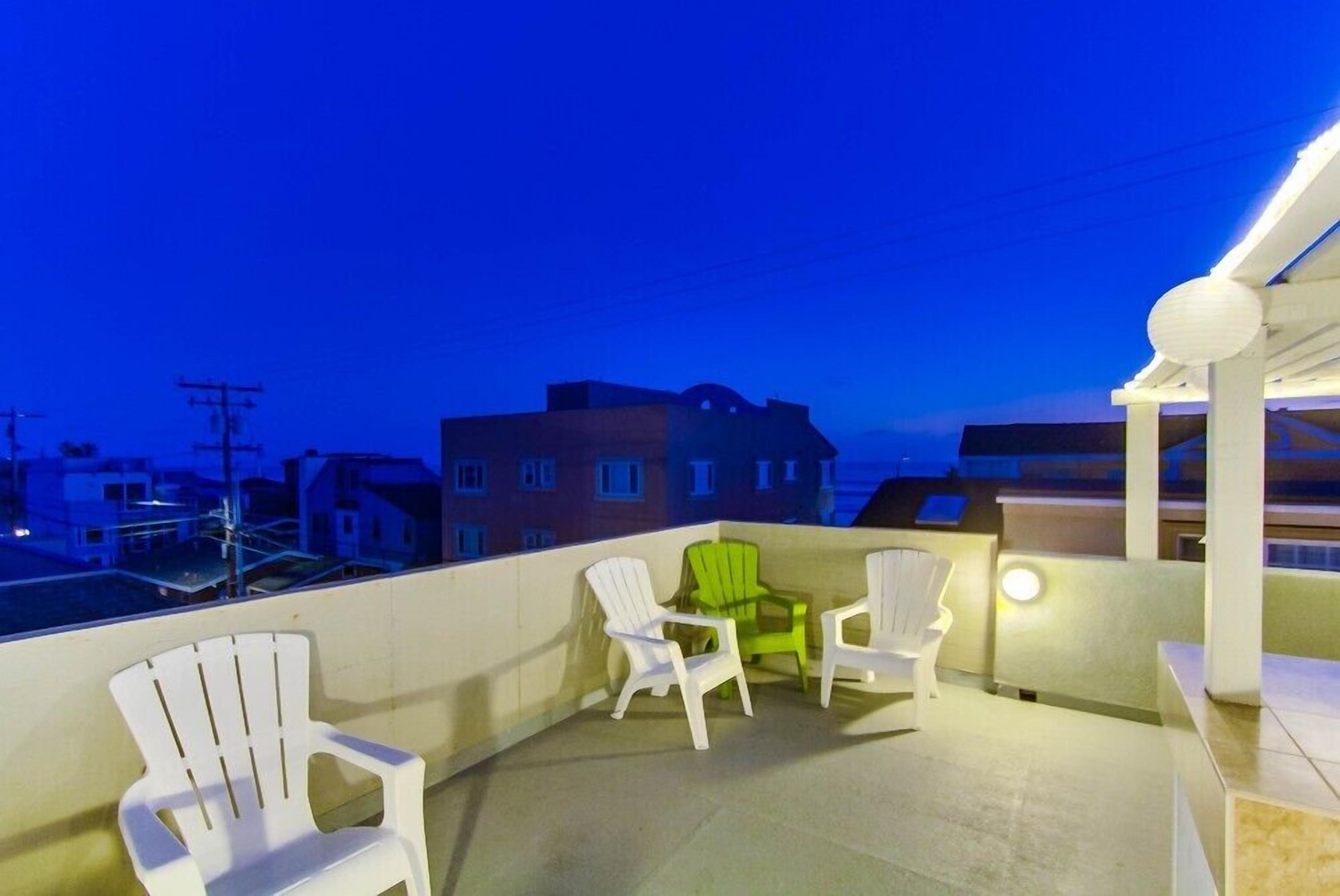 A balcony with white and green Adirondack chairs, a small table, and a view of buildings in the background.