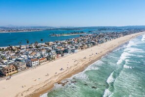 A coastal cityscape with a long beach, clear blue waters, and a dense urban area with buildings.