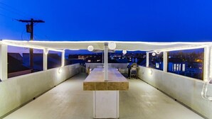 Una terraza exterior con una mesa y sillas, rodeada por una barandilla blanca, bajo un cielo despejado.