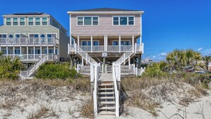 A beachfront property with a wooden staircase leading to a balcony, surrounded by sand and sparse vegetation. - Against The Wind Side B, Oceanfront Home, Awesome view of Garden City Pier (Garden City Beach)