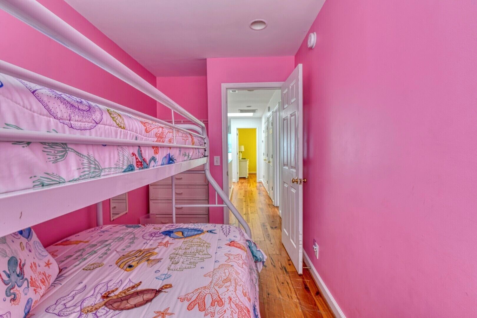 A bunk bed room with pink walls and a hallway leading to a door.