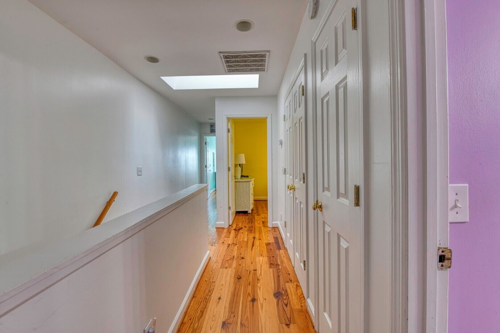 A hallway with wooden flooring, white walls, and a yellow door at the end.