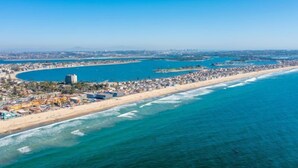 Vista aérea de una ciudad costera con una extensa playa, aguas azules cristalinas y una zona urbana densa con edificios e infraestructura.