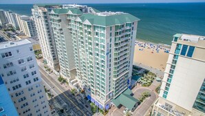 A high-rise hotel with multiple floors, a green roof, and a view of the beach.